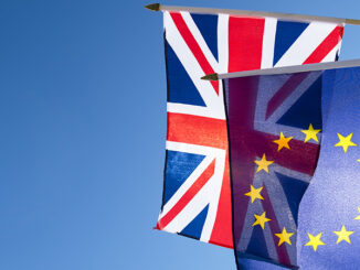Low-angle view of European Union flag and British flag flying in front of bright blue sky