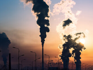 silhouette of a high industrial pipe with the sun behind it