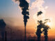 silhouette of a high industrial pipe with the sun behind it
