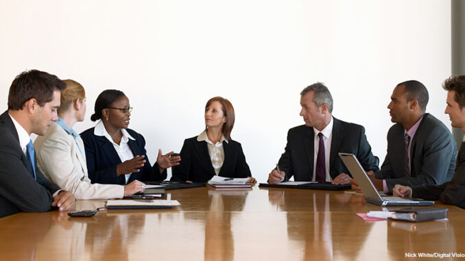 Business people in meeting looking at woman making hand gestures Business men and business women in meeting around conference table.