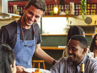 Cheerful male chef serving couple in restaurant