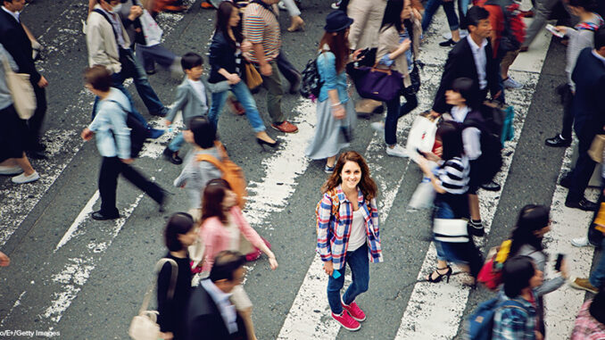Young caucasian girl is smiling confused losted in Tokyo crowd woman standing in crowd of pedestrians