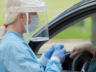 medical personnel in protective clothing and face shield encounters a person in a car during a COVID-19 test