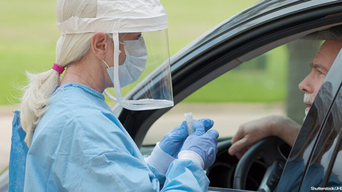 060120_01P_FS medical personnel in protective clothing and face shield encounters a person in a car during a COVID-19 test