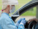 medical personnel in protective clothing and face shield encounters a person in a car during a COVID-19 test