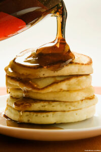 Pouring maple syrup over pancakes