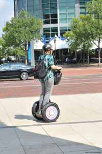 profile view of a woman riding a Segway (personal transportation vehicle) on a city sidewalk