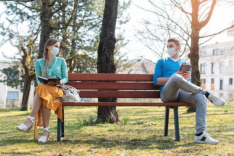 Woman and man in social distancing sitting on bench in park; 