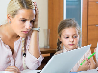 Tired woman irritated as her preschooler daughter diverts her from work at home