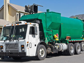 Garbage truck emptying a trash bin in front of a house.