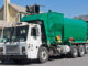 Garbage truck emptying a trash bin in front of a house.