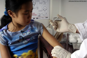 A young girl being given a vaccine shot in the arm by a doctor.