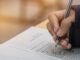student hands taking exams, writing examination on paper answer sheet