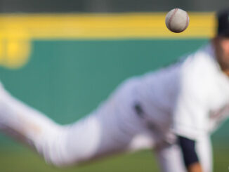 A baseball in motion with pitcher in background.