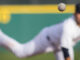 A baseball in motion with pitcher in background.