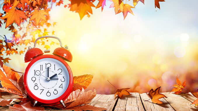 Daylight Savings Time Concept - Clock And Leaves On Wooden Table alarm clock on autumnal background