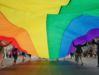 People Holding Large Colorful Flag While Walking