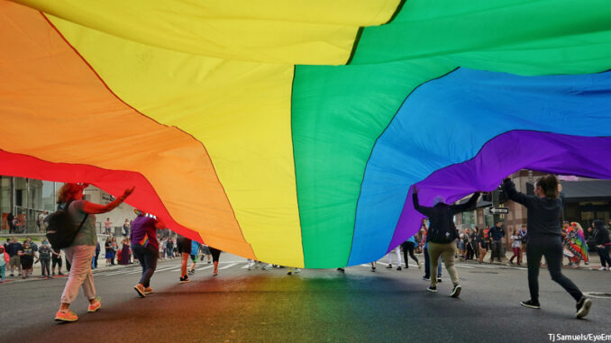 People Holding Large Colorful Flag While Walking On City Street People Holding Large Colorful Flag While Walking