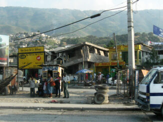Haitians standing near a earthquake-damaged building
