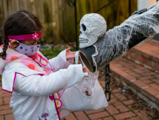 girl in doctor costume socially distant trick or treating candy chute
