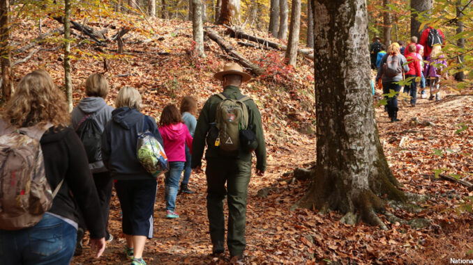 A youth group enjoys fall foliage on a ranger walk in the Great Smoky Mountains National Park A park ranger leads a group of people in a forest walk.