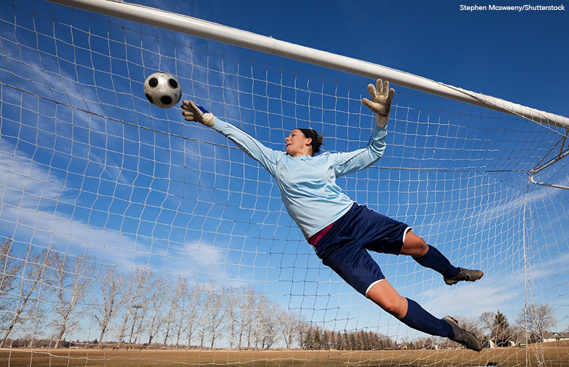 A female soccer goalie diving to catch the ball in front of a soccer net