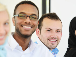 four multi-ethnic people in a row, smiling at the camera, two women in hijab