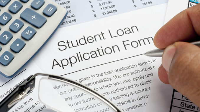 Student Loan application Form with pen, calulator and writing h overhead view of a man's hand poised with a pen above a sheet of paper reading 'Student Loan Application Form'.