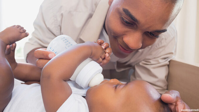 Happy father feeding his baby boy at home in the bedroom father feeding his baby from a bottle