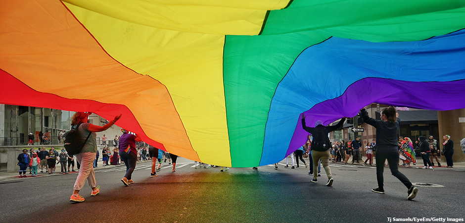 People Holding Large Rainbow Pride Flag While Walking On City Street