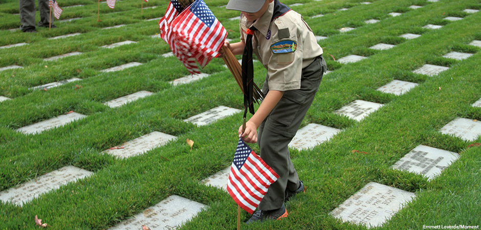 A Boy Scout places an American Flag at the grave marker of a US soldiers at the Los Angeles National Cemetery.