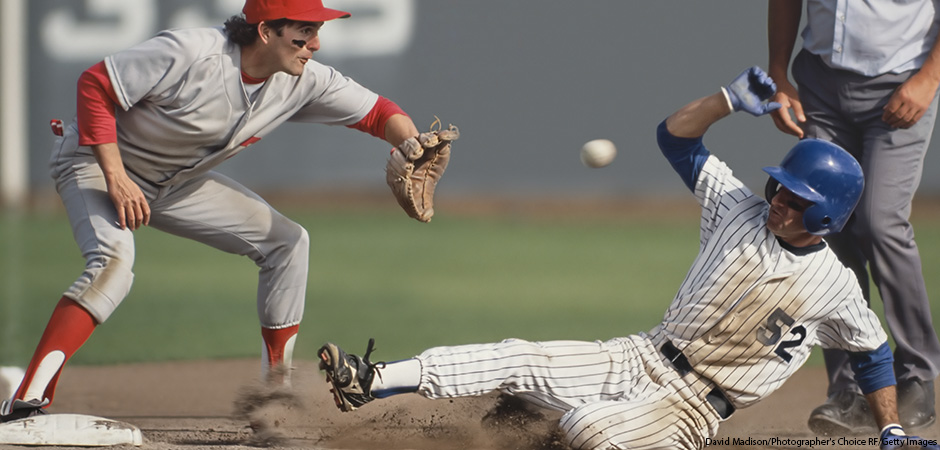 Baseball player sliding into third base with umpire behind him and fielder in process of catching ball.