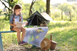 Little girl with map and book near tent outdoors.
