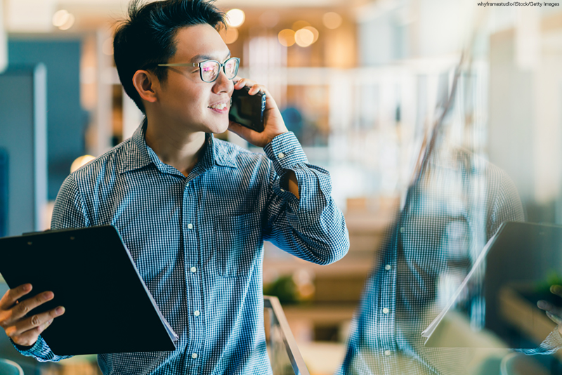 A young Asian entrepreneur using a smartphone working in office background.