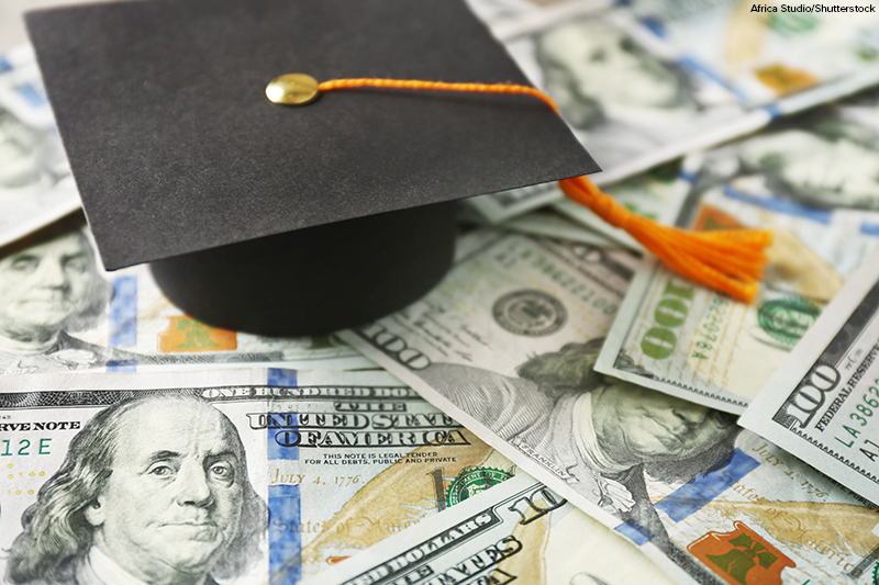Close up view of graduation hat on dollar banknotes. Tuition fees concept;