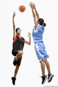 Full-length view of two mixed-race women playing basketball, both reaching for the ball against a white background