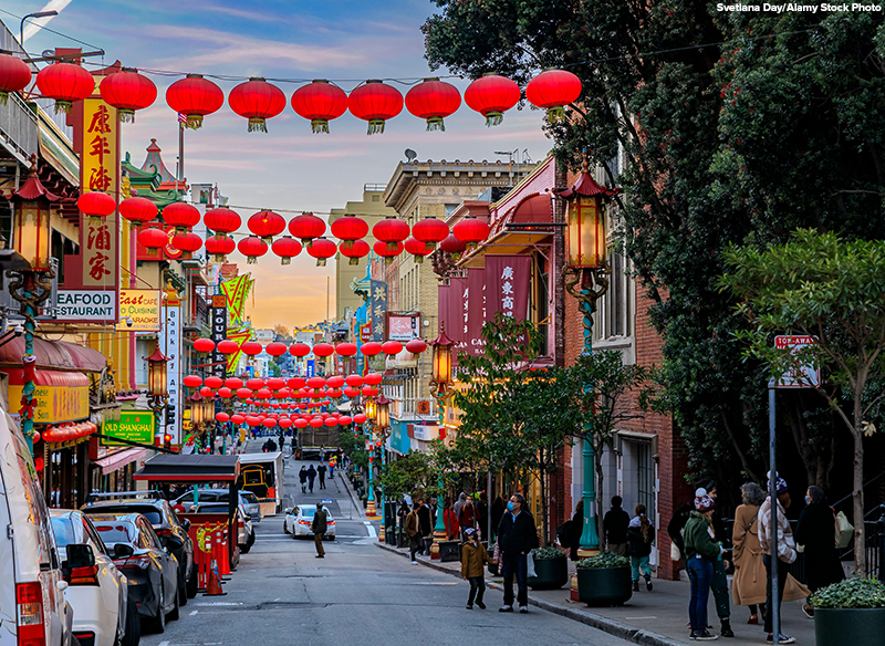 Traditional shops, lanterns and people in the street in Chinatown near downtown San Francisco, California with a fiery sunset