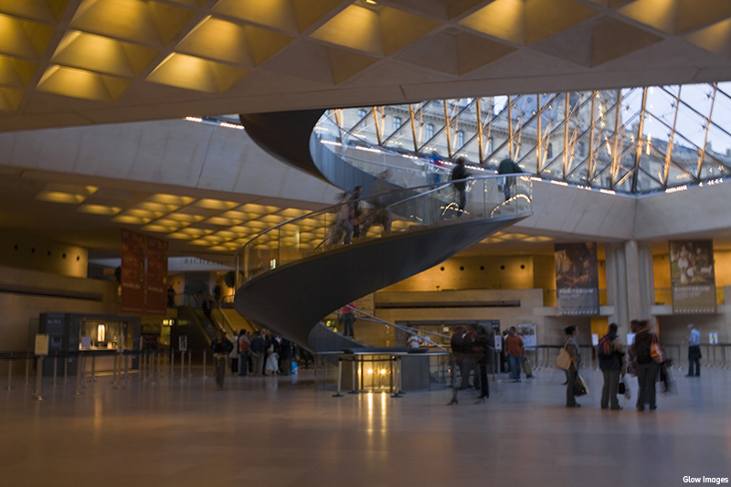 Interior view the Louvre Pyramid of the Louvre Museum with spiral staircase and tourists, Paris, France.