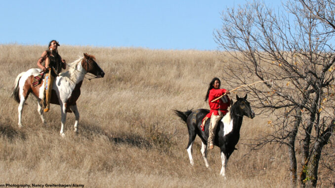Two Native American Indians riding horseback through the prairie of South Dakota.