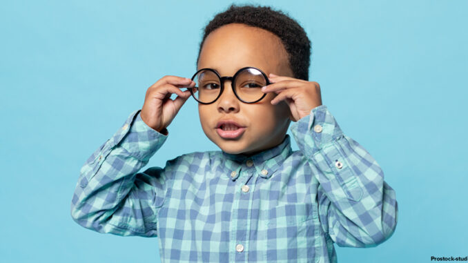Portrait of little black boy wearing eyeglasses looking at camera, standing on blue studio background.