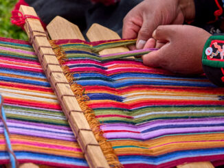 The hands of a weaver operating a loom with colorful thread.