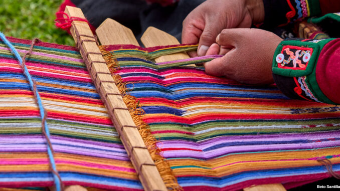 The hands of a weaver operating a loom with colorful thread.